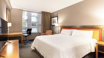 A hotel room with a bed, desk, chair, and a window with curtains.