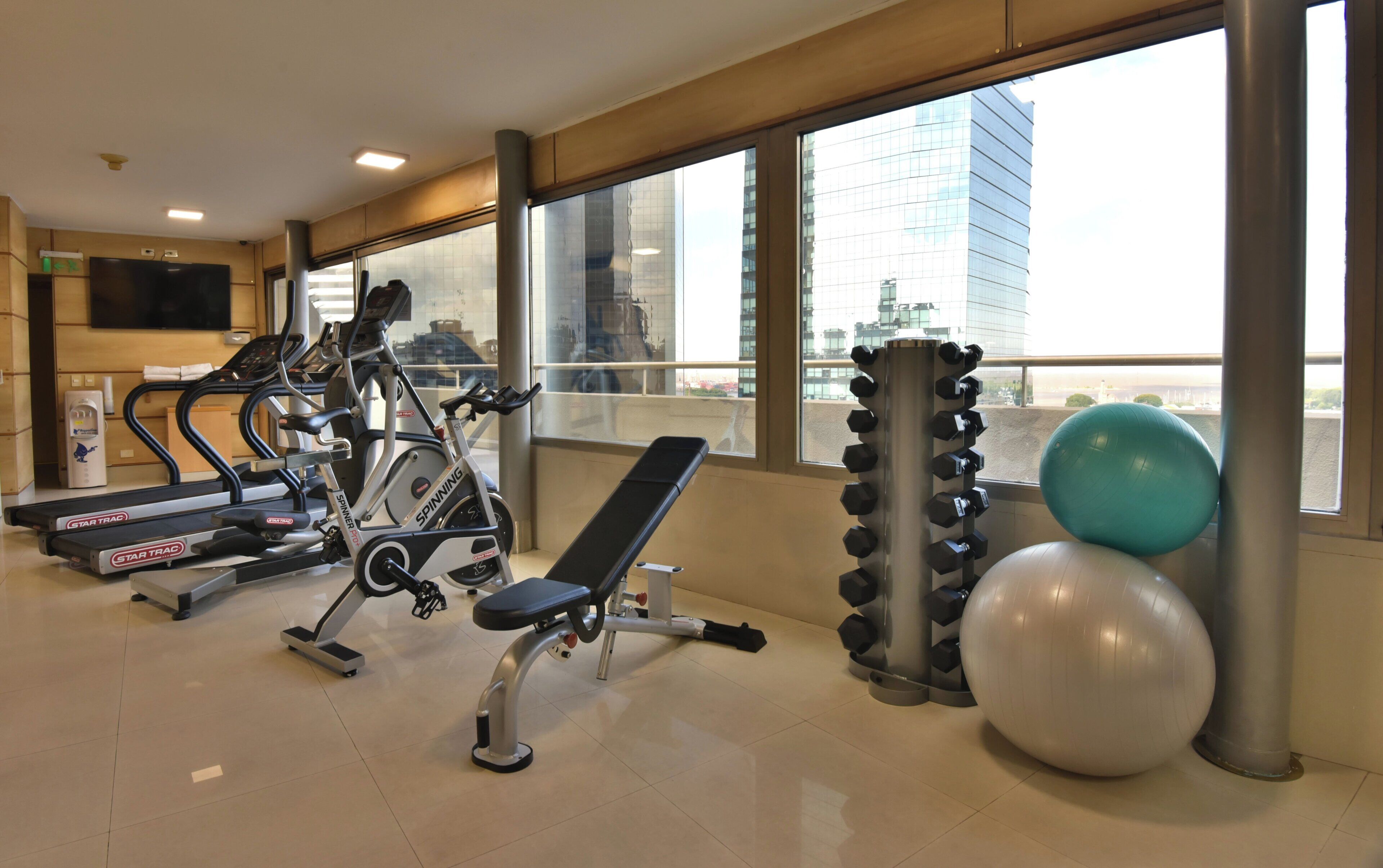 Academia com equipamentos de ginástica, um banco, halteres e bolas de exercício.