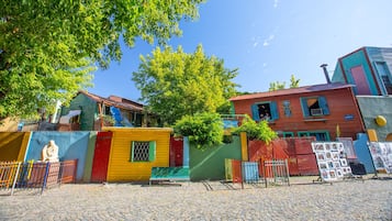 Rua de paralelepípedos com edifícios coloridos, um banco e uma cerca com imagens.