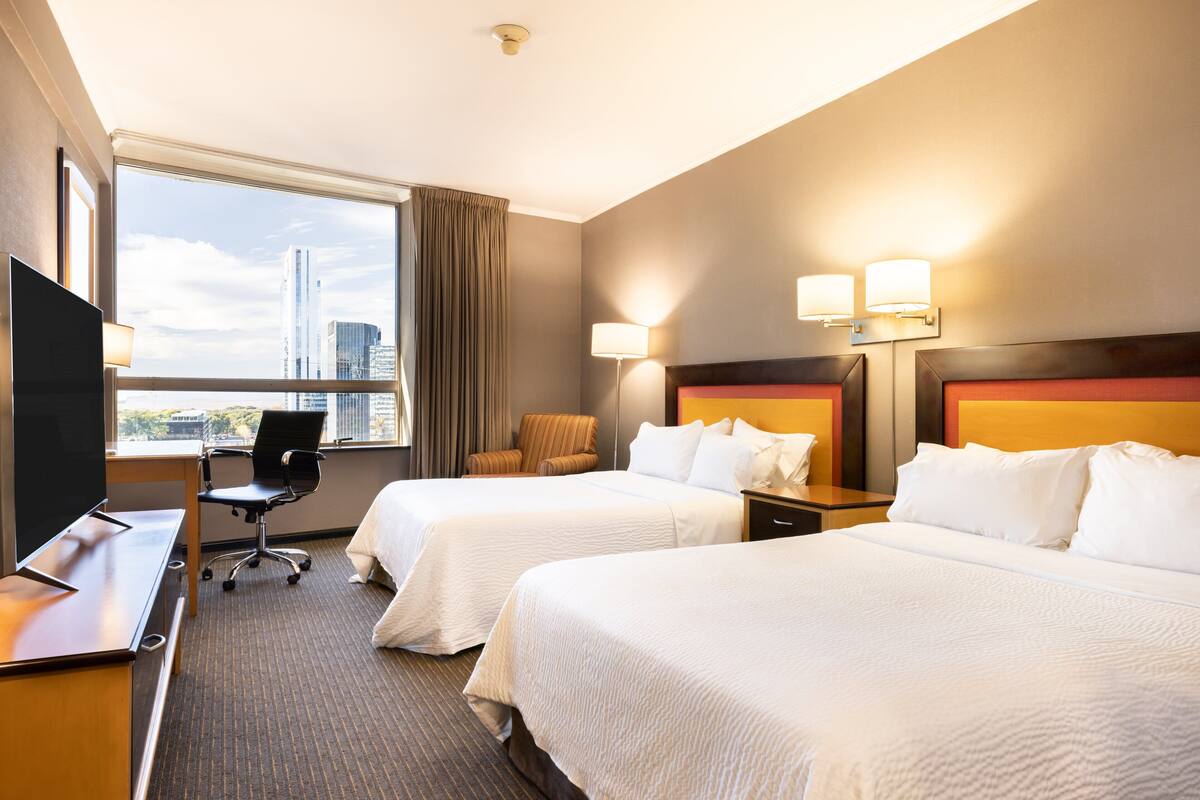 A hotel room with two beds, a desk, a chair, and a TV.