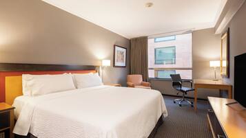A hotel room with a large bed, a desk, a chair, and a television.
