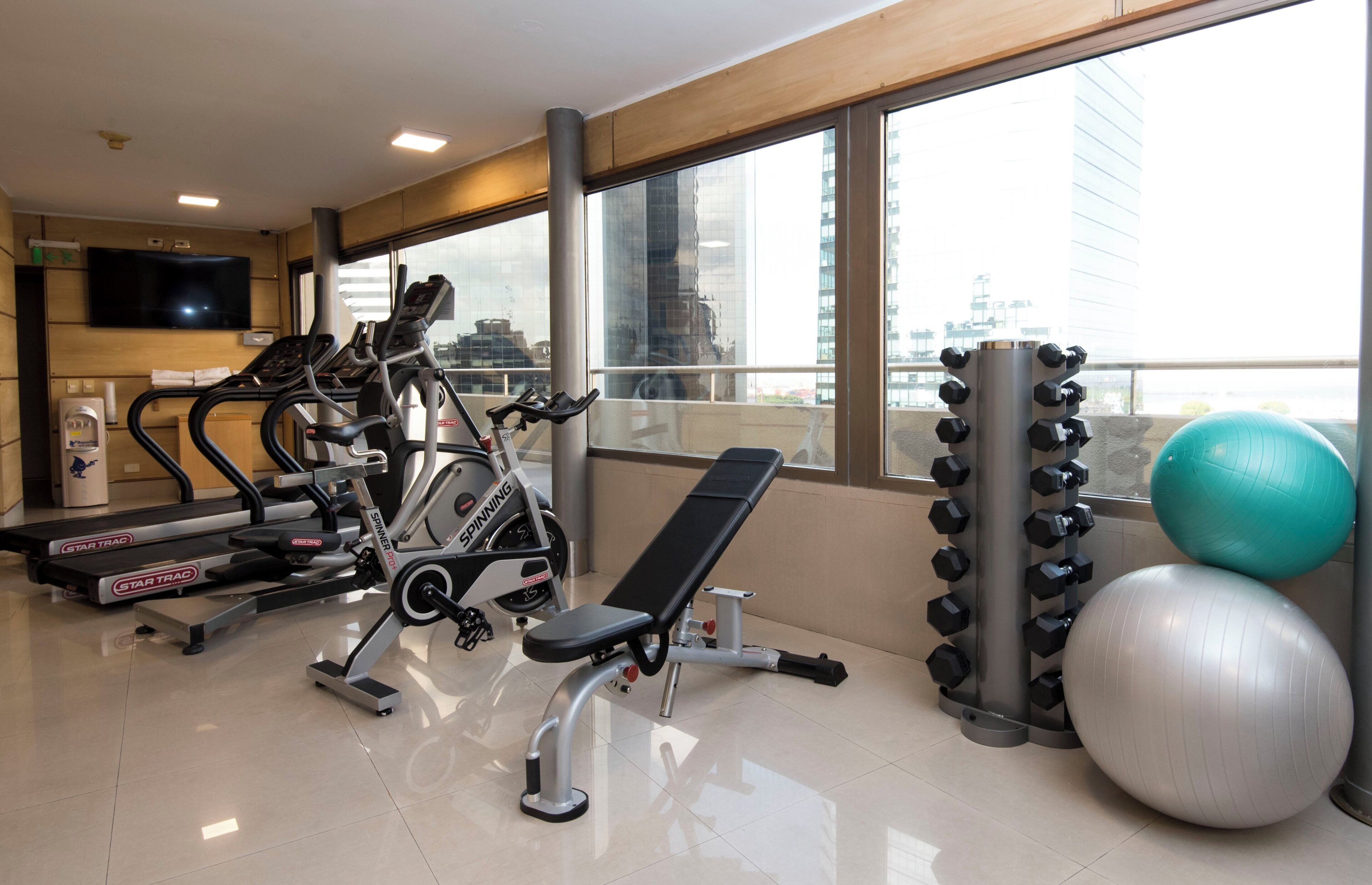 Une salle de sport équipée de machines de cardio, d’un banc de musculation, de piles de poids et de ballons d’exercice.