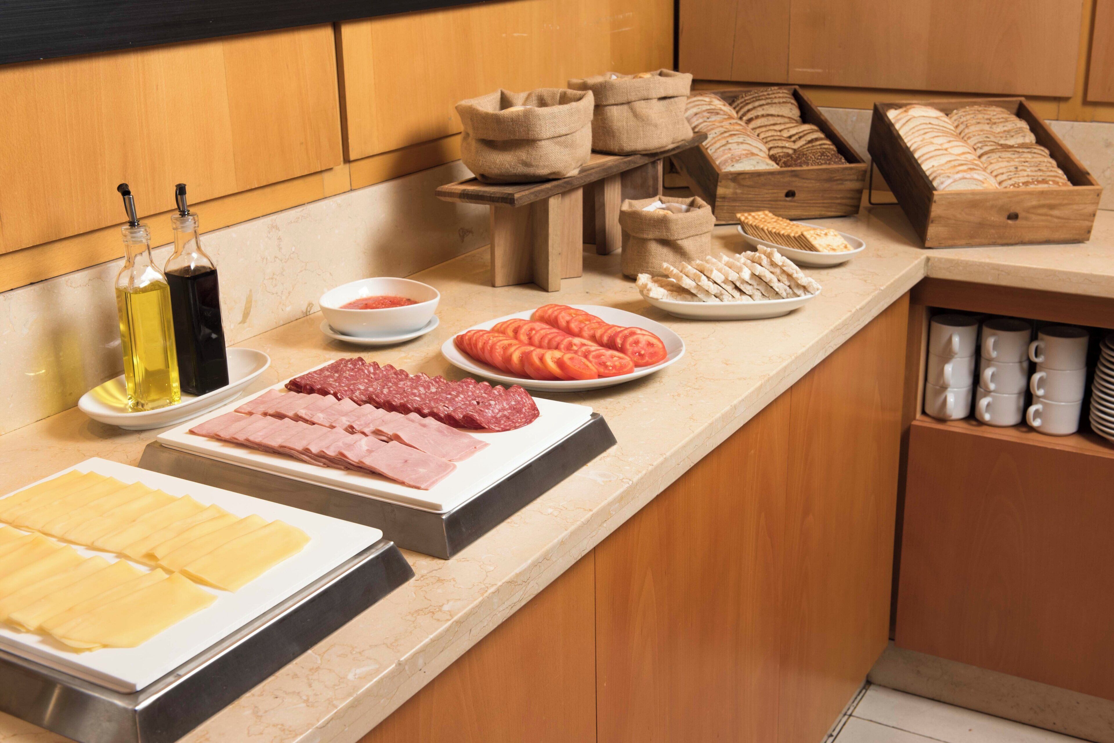 A buffet setup with various food items including sliced meats, cheeses, and bread.