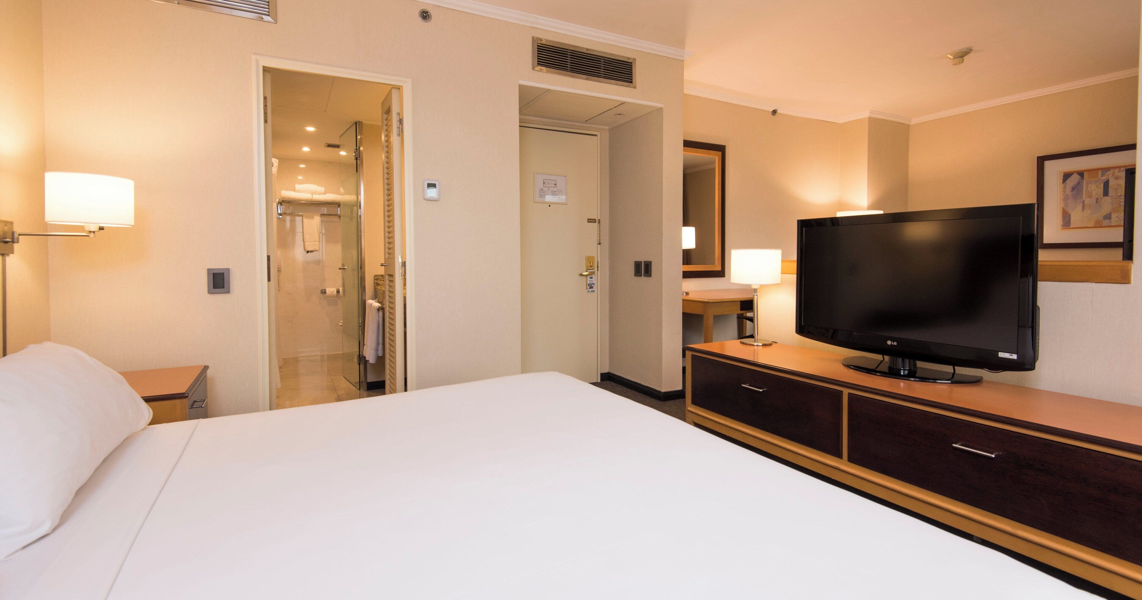 Ett hotellrum med en säng, en tv, ett skrivbord och ett badrum som syns genom en öppen dörr.