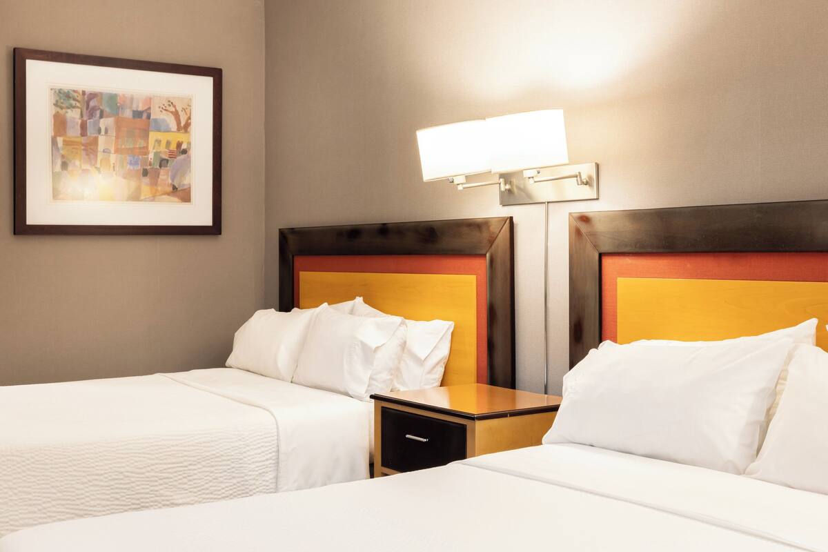 A hotel room with two beds, a nightstand, a framed picture on the wall, and a wall-mounted light fixture.