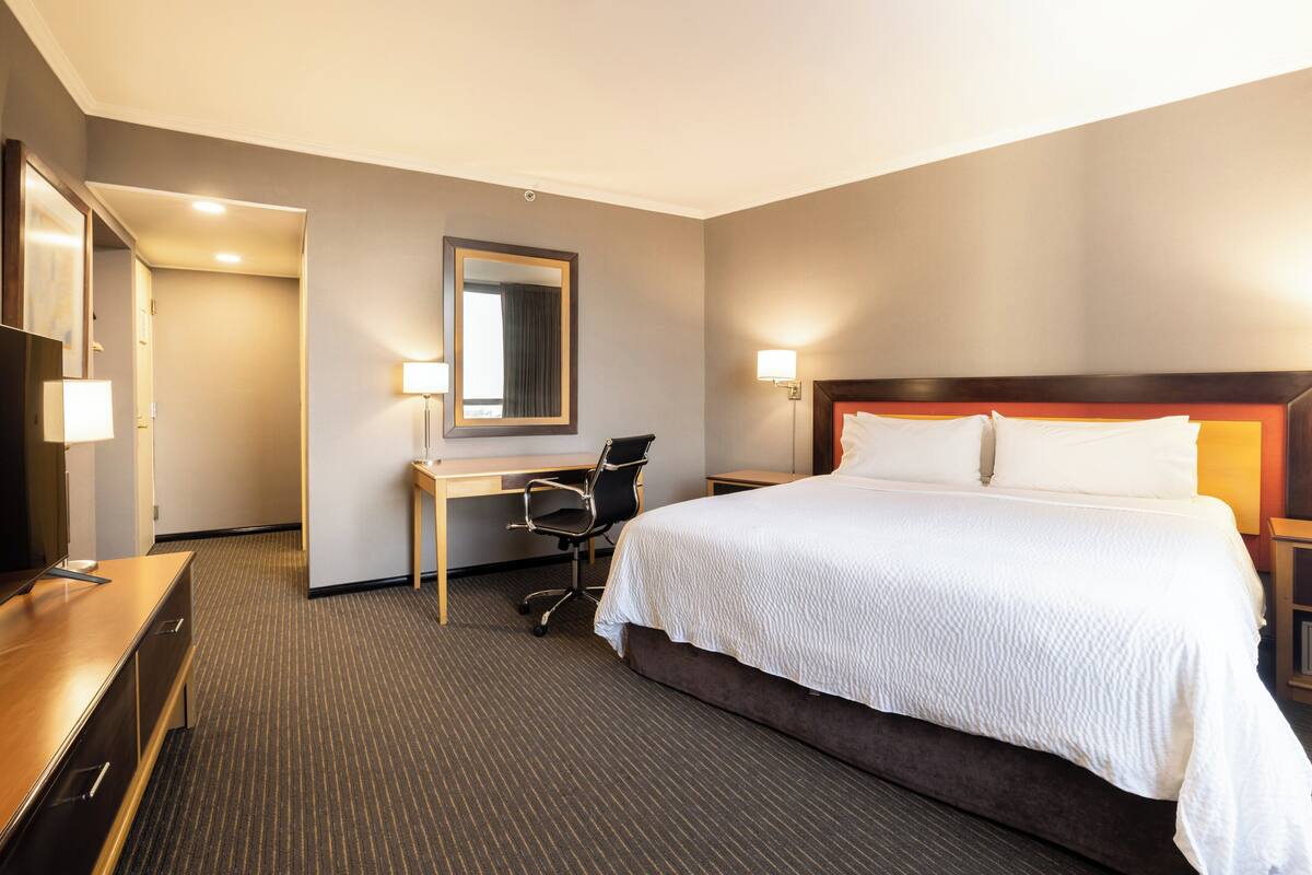 A hotel room with a large bed, a desk, a chair, a TV, and a mirror.
