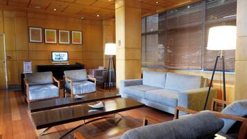A hotel lobby with a seating area, a television, and a large window with blinds.