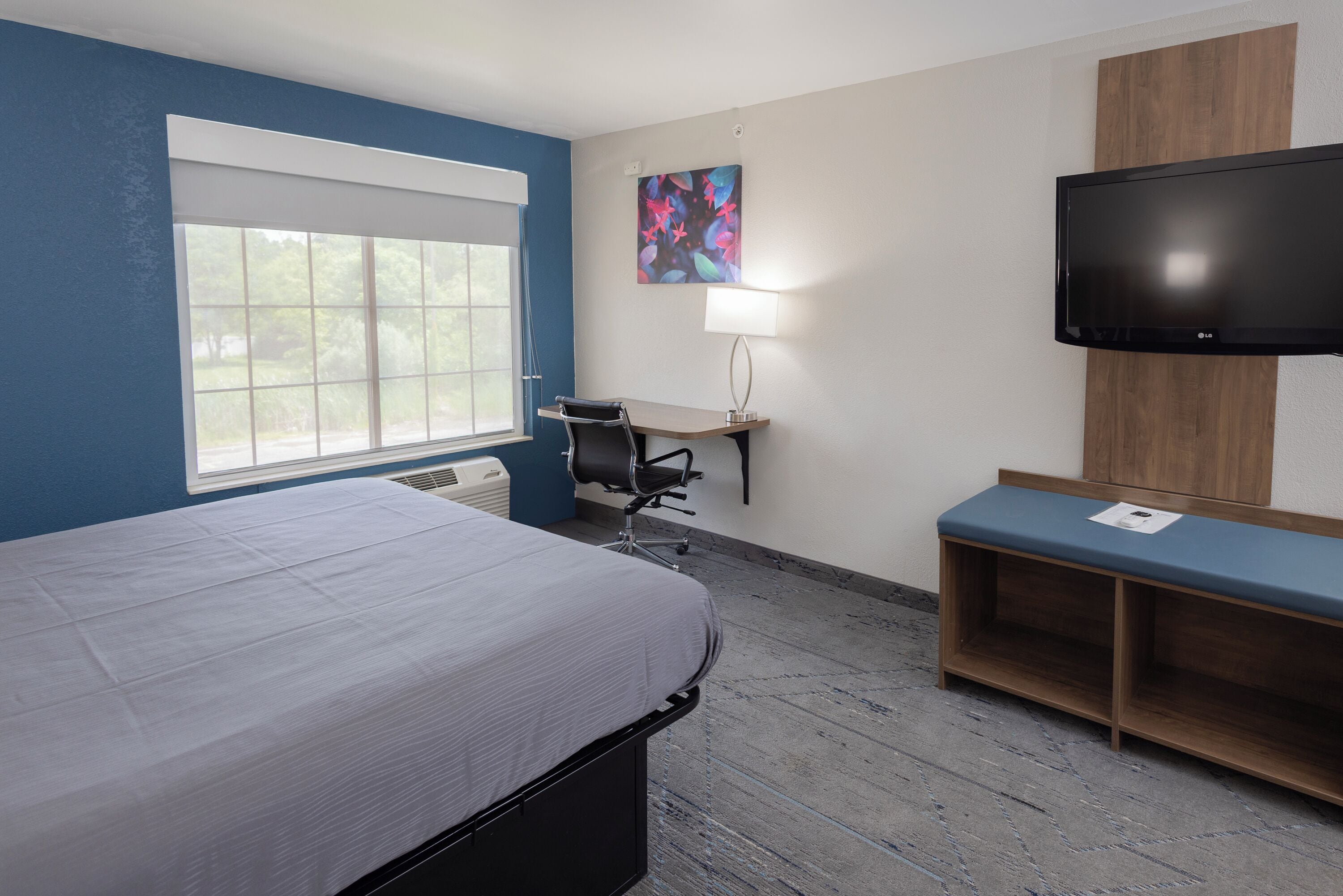 A hotel room with a bed, desk, chair, TV, and a window.