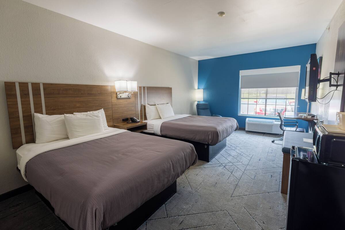 Habitación de hotel con dos camas, un escritorio, una silla, un televisor y una ventana con vistas a coches.
