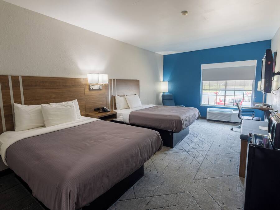 Hotellihuone, jossa on kaksi sänkyä, työpöytä, tuoli, televisio ja ikkuna, josta on näkymä kadulle ja ohikulkeviin autoihin.