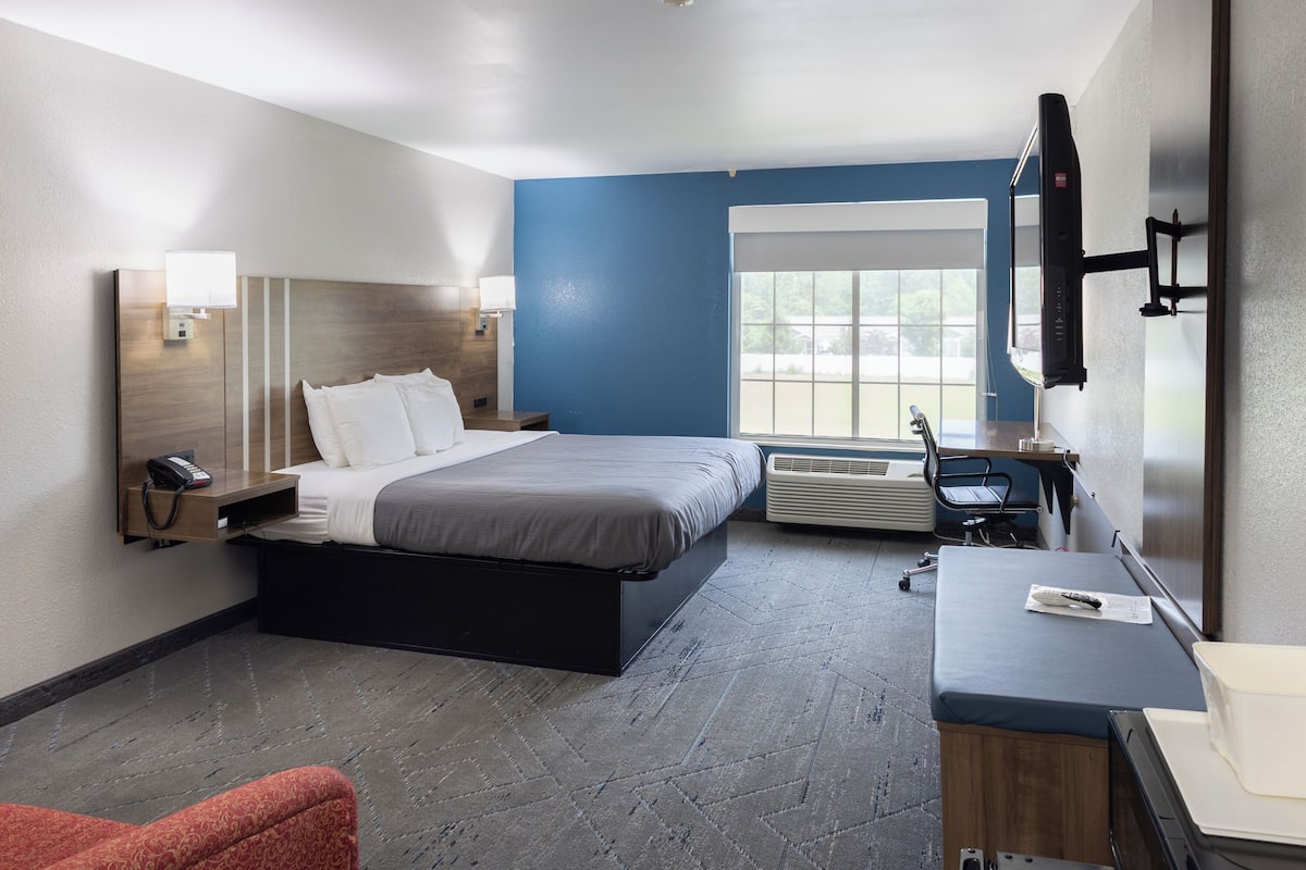 Una habitación de hotel con cama, mesita de noche, lámpara, televisión y escritorio con silla.