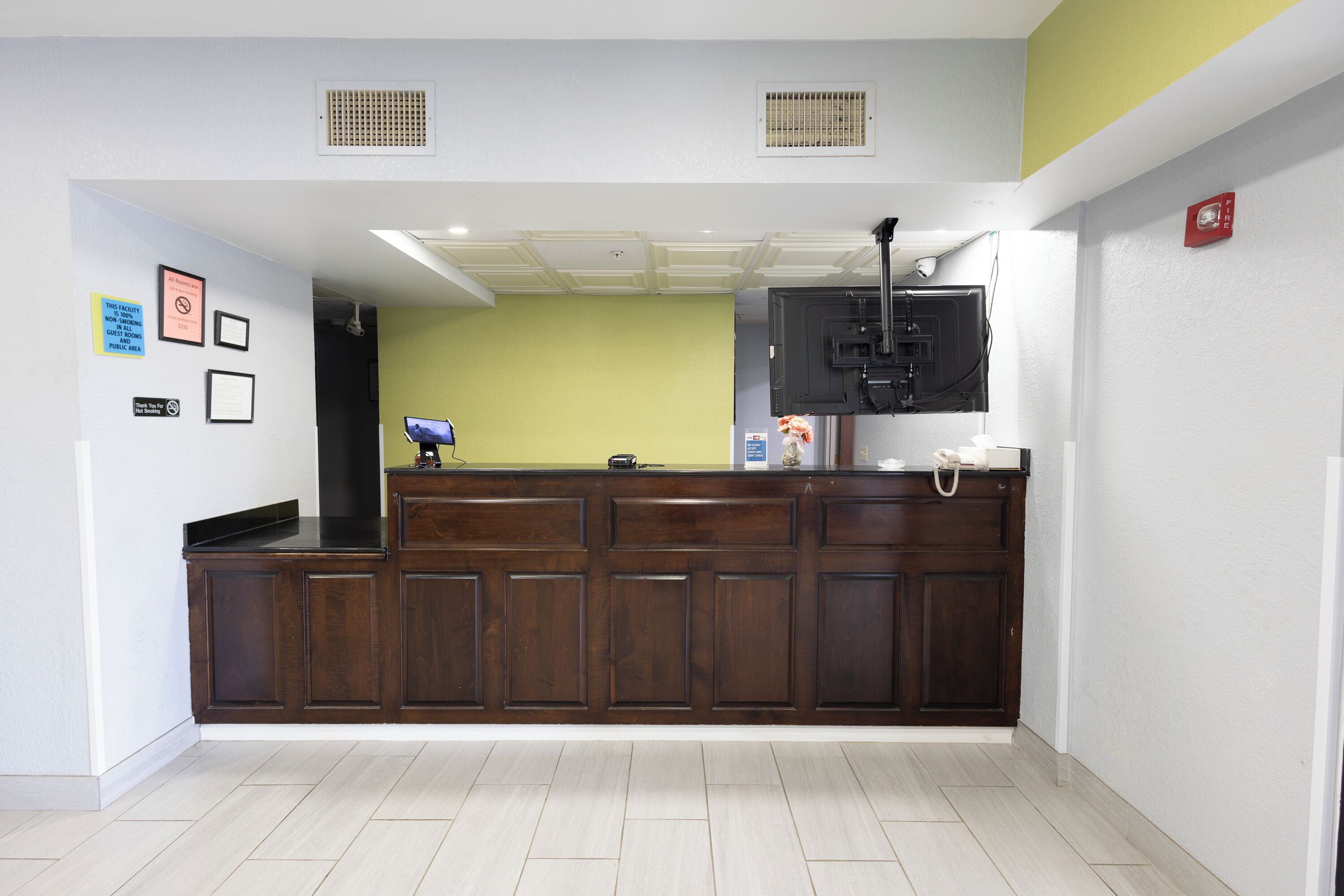 A reception area with a dark wooden counter, a flat-screen TV mounted above it, and a fire alarm on the wall.