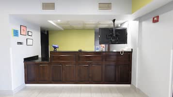 A reception area with a dark wooden counter, a flat-screen TV mounted above it, and a fire alarm on the wall.