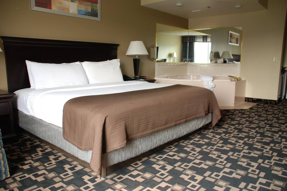 Une chambre d’hôtel avec un grand lit, une lampe de chevet, une salle de bain avec baignoire et une moquette à motifs.