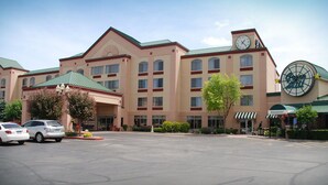 Un hôtel doté d’une tour centrale avec une horloge, de nombreuses fenêtres et d’un parking rempli de voitures.