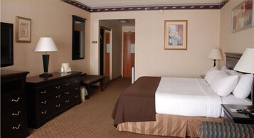 Habitación de hotel con cama, mesitas de noche, cómoda, lámpara y puerta que da a otra habitación.