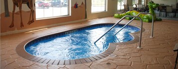 Una piscina interior con borde de azulejos, una escalera y vistas al exterior a través de amplias ventanas.