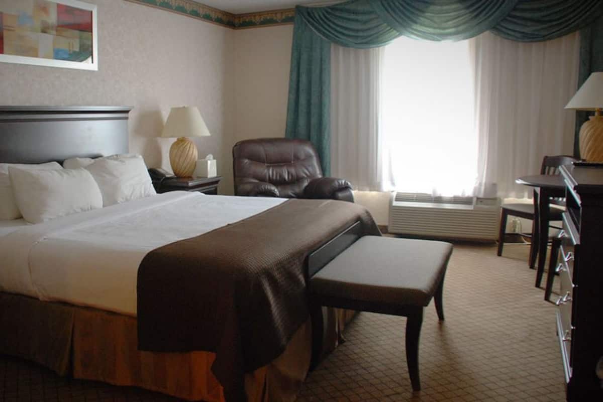 Une chambre d’hôtel avec un grand lit, une chaise, un bureau et une fenêtre avec des rideaux.