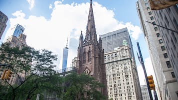 Uma igreja histórica com uma torre alta, cercada por arranha-céus modernos e árvores.
