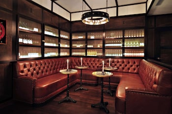 A modern hotel room with a glass coffee table, two armchairs, a sofa, a kitchen area with bar stools, and a large window with curtains. at Gild Hall, A Thompson Hotel, by Hyatt
