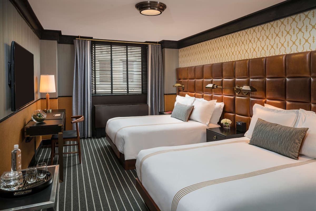 Une chambre d’hôtel avec deux lits, un bureau, une chaise, une télévision et une fenêtre avec des rideaux.