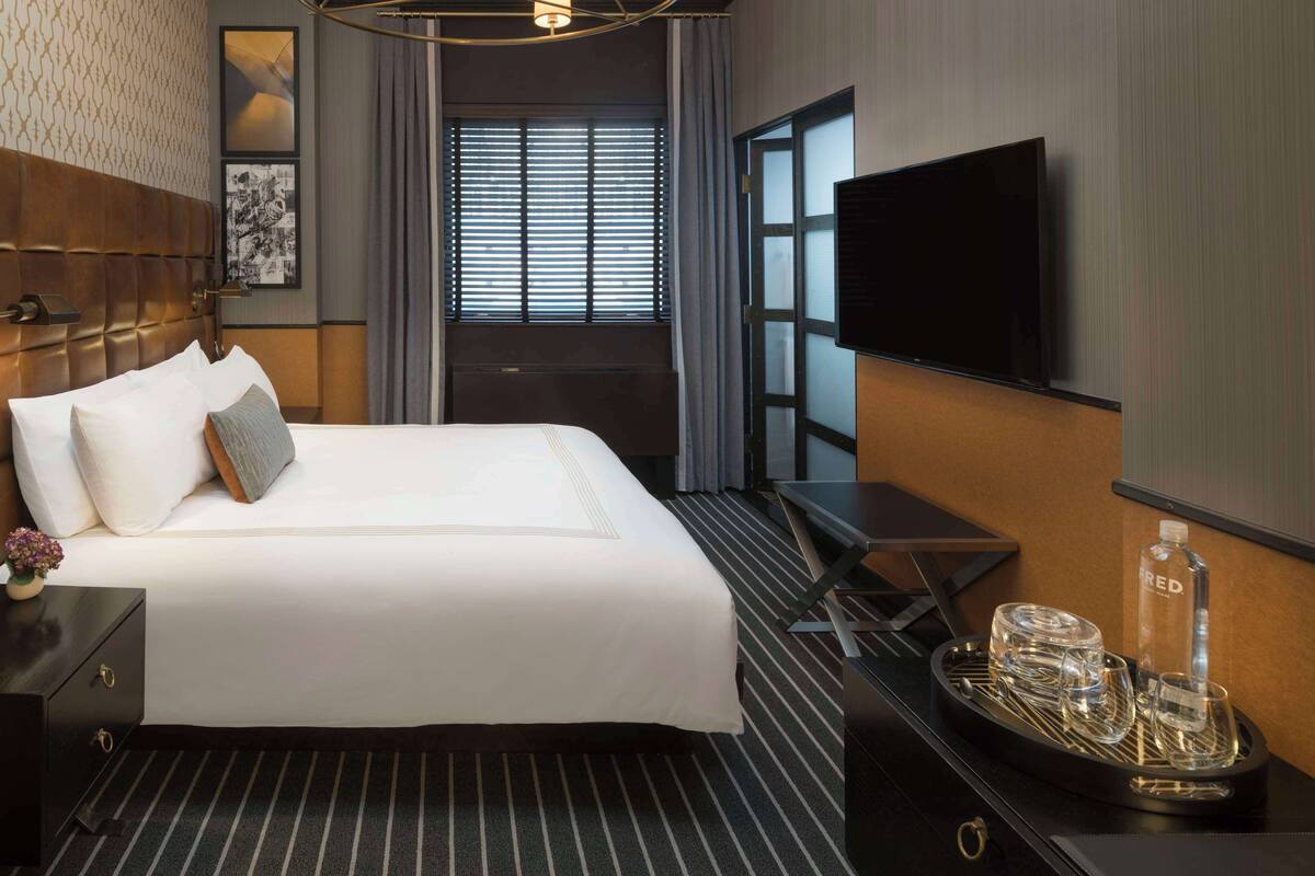 Une chambre d’hôtel avec un grand lit, un téléviseur à écran plat, un bureau avec un plateau de verres et une fenêtre équipée de stores.