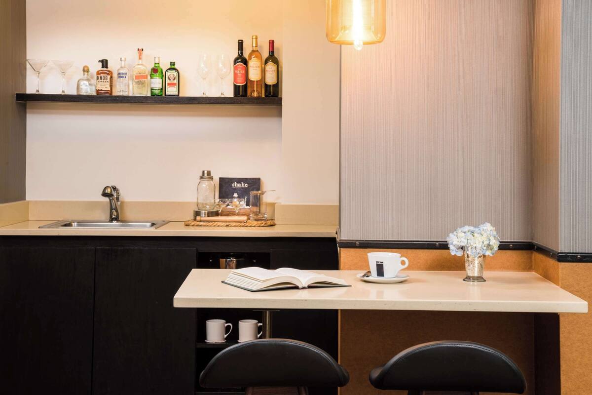 Une cuisine moderne dotée d’un évier encastré, d’une machine à café, d’une étagère contenant diverses bouteilles et d’un petit coin repas avec deux chaises et une table.
