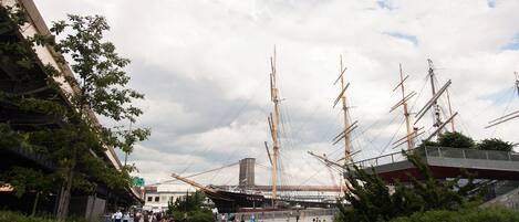 Un paseo marítimo frente al agua con un gran barco velero amarrado, un puente moderno y un edificio con techo inclinado.