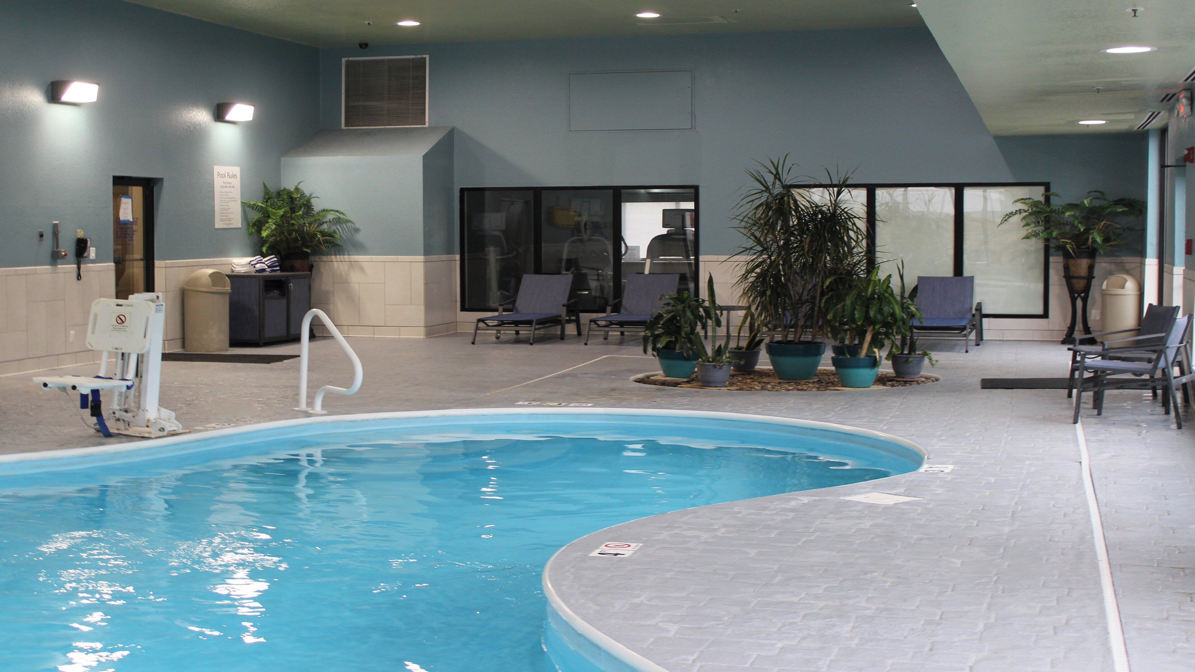 Una piscina interior con un elevador de piscina, sillones de descanso y plantas en macetas.