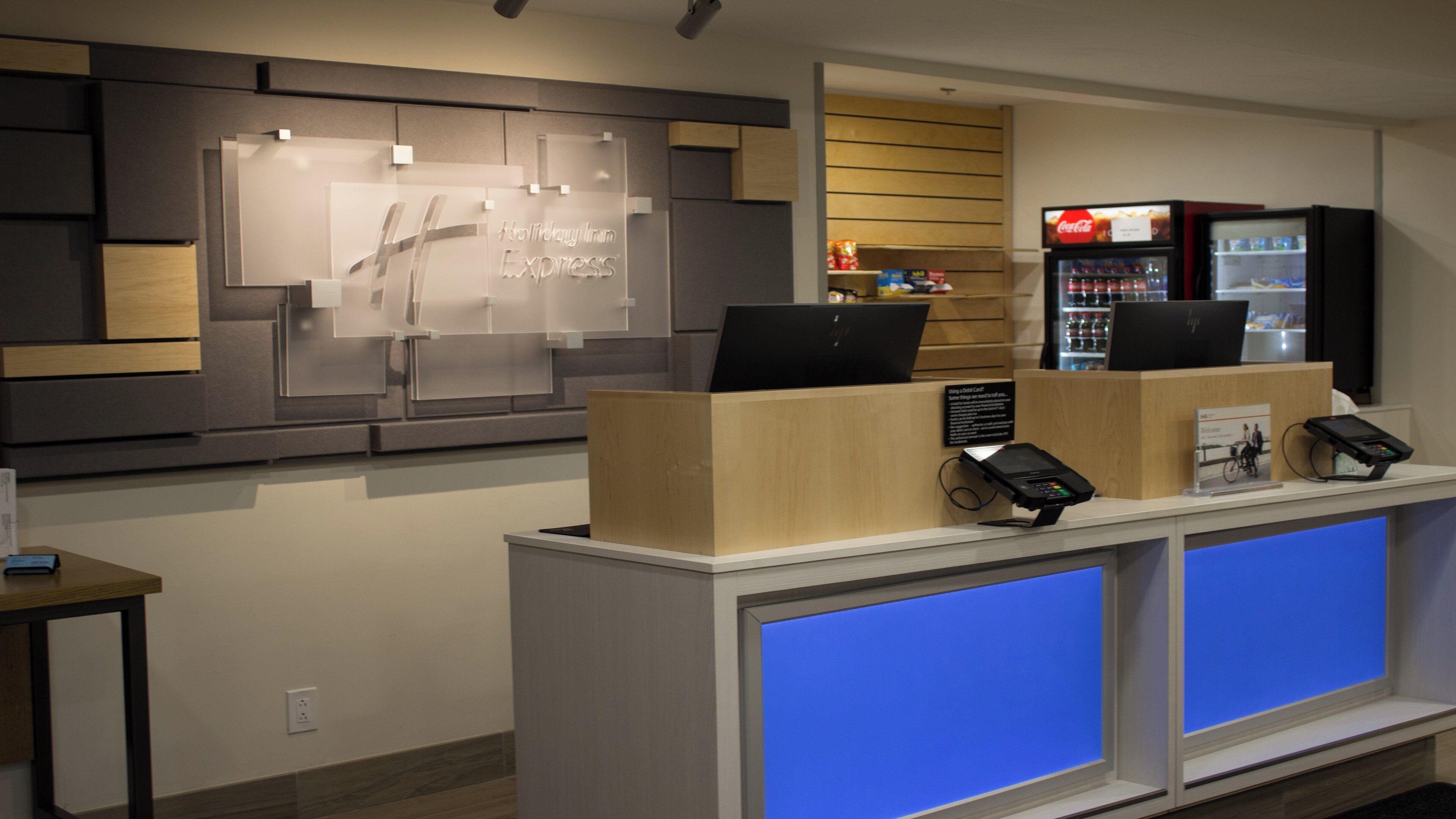 Uma receção de hotel com um ecrã digital, um frigorífico de Coca-Cola e um sinal para Holiday Inn Express.