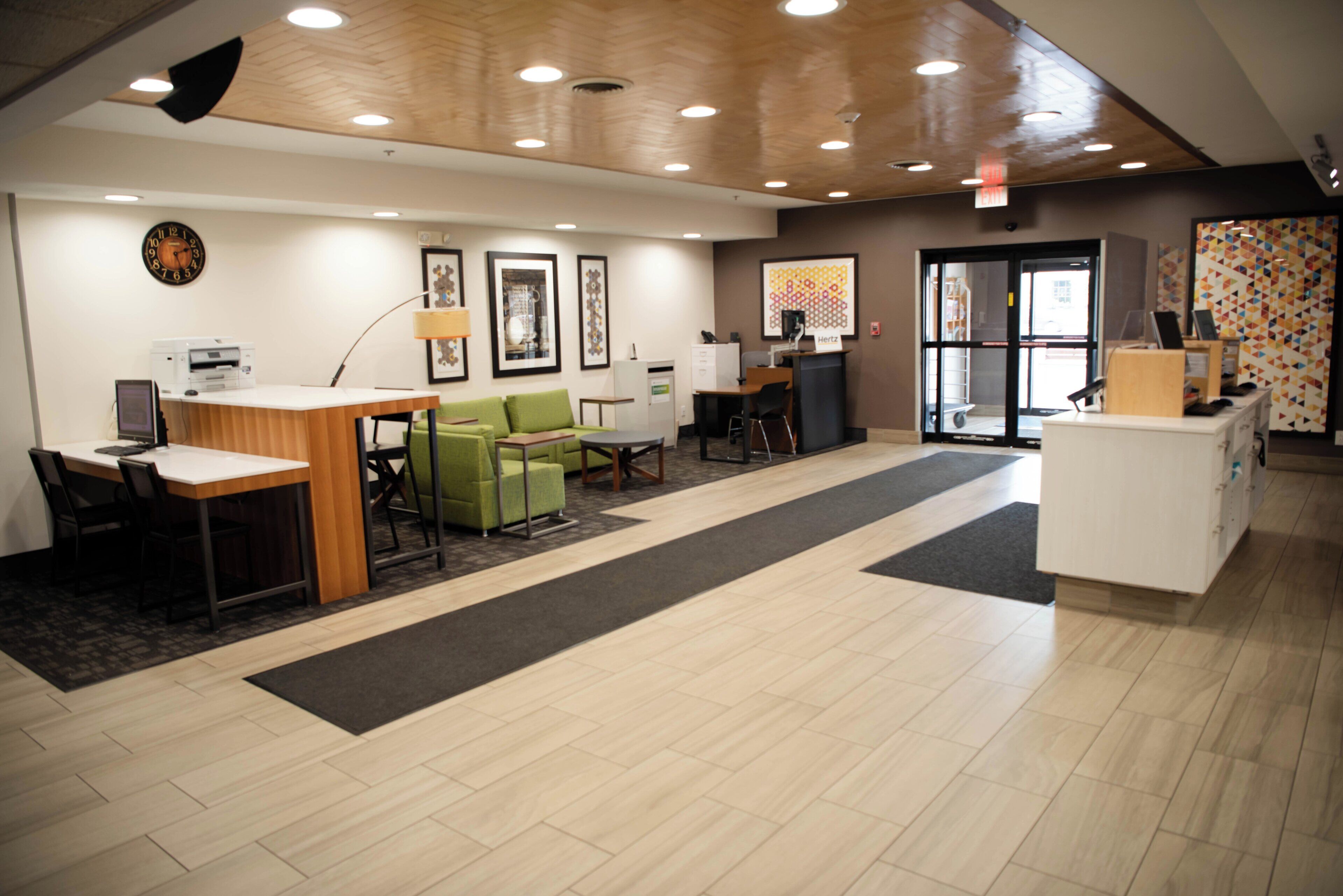A spacious lobby with a reception desk, green seating area, and a large clock on the wall.