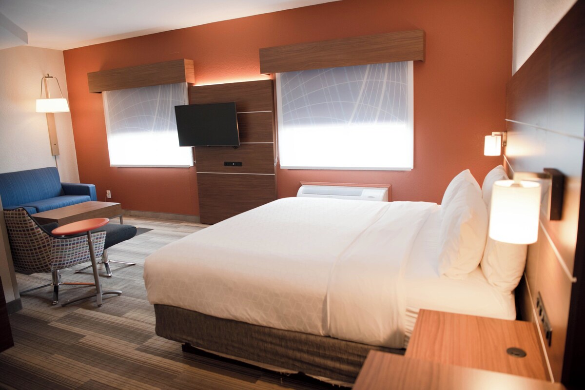 A hotel room with a bed, a desk, a chair, a TV, and a window with curtains.