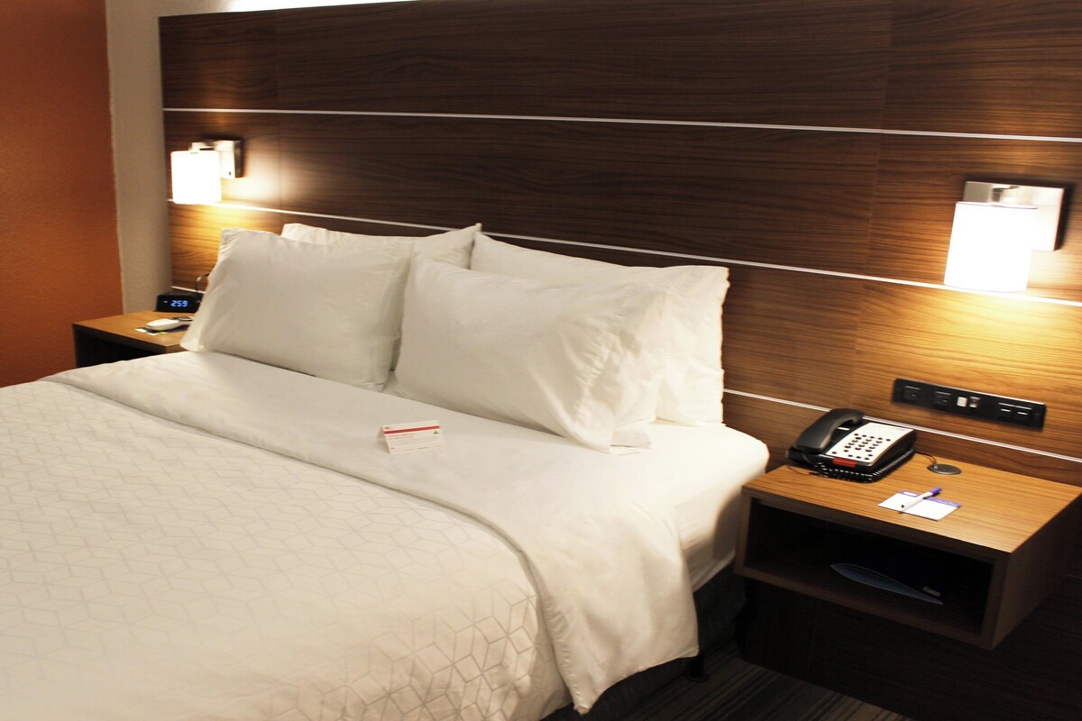 A hotel room with a neatly made bed, a bedside phone, and a nightstand with a lamp.