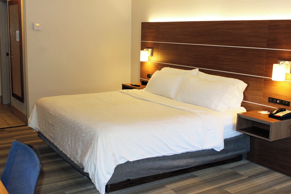 A hotel room with a large bed, wooden headboard, bedside lamps, and a nightstand with a phone.