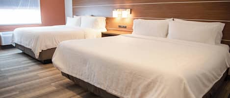 A hotel room with two beds, a wooden headboard, a nightstand with a lamp, and a window with blinds.
