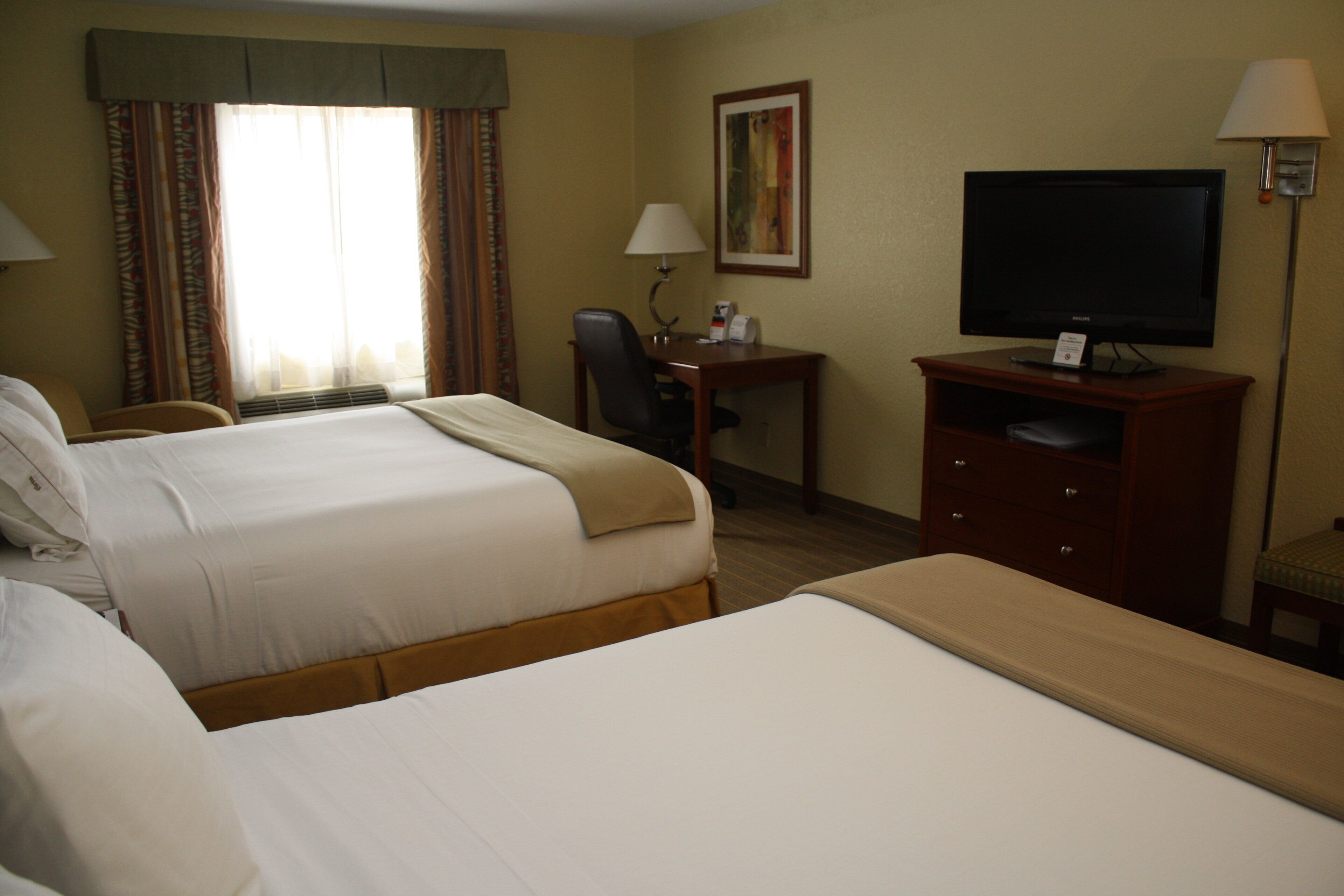 A hotel room with two beds, a desk with a chair, a television, and a lamp.