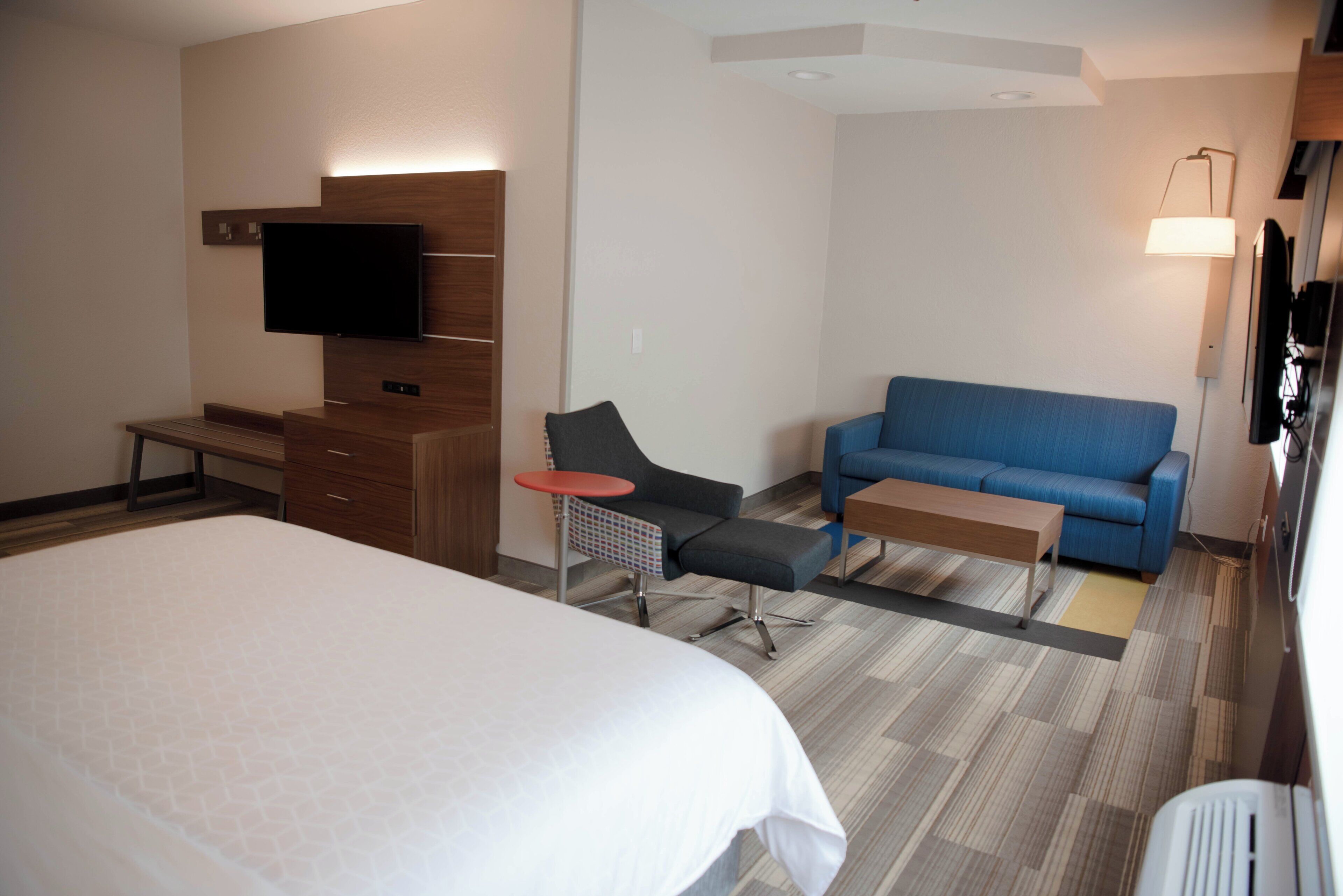 A hotel room with a large bed, a desk, a chair, a sofa, a TV, and a lamp.