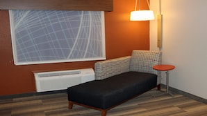 A small room with a single sofa, a patterned chair, a small table, a radiator, and a window with a geometric pattern. - Holiday Inn Express Winfield by IHG (Hurricane)