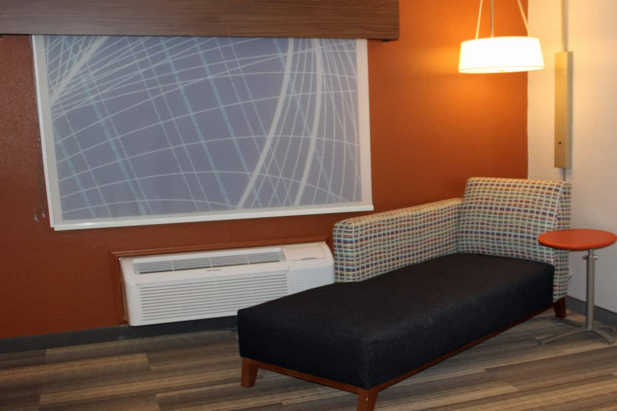 A small room with a single sofa, a patterned chair, a small table, a radiator, and a window with a geometric pattern.
