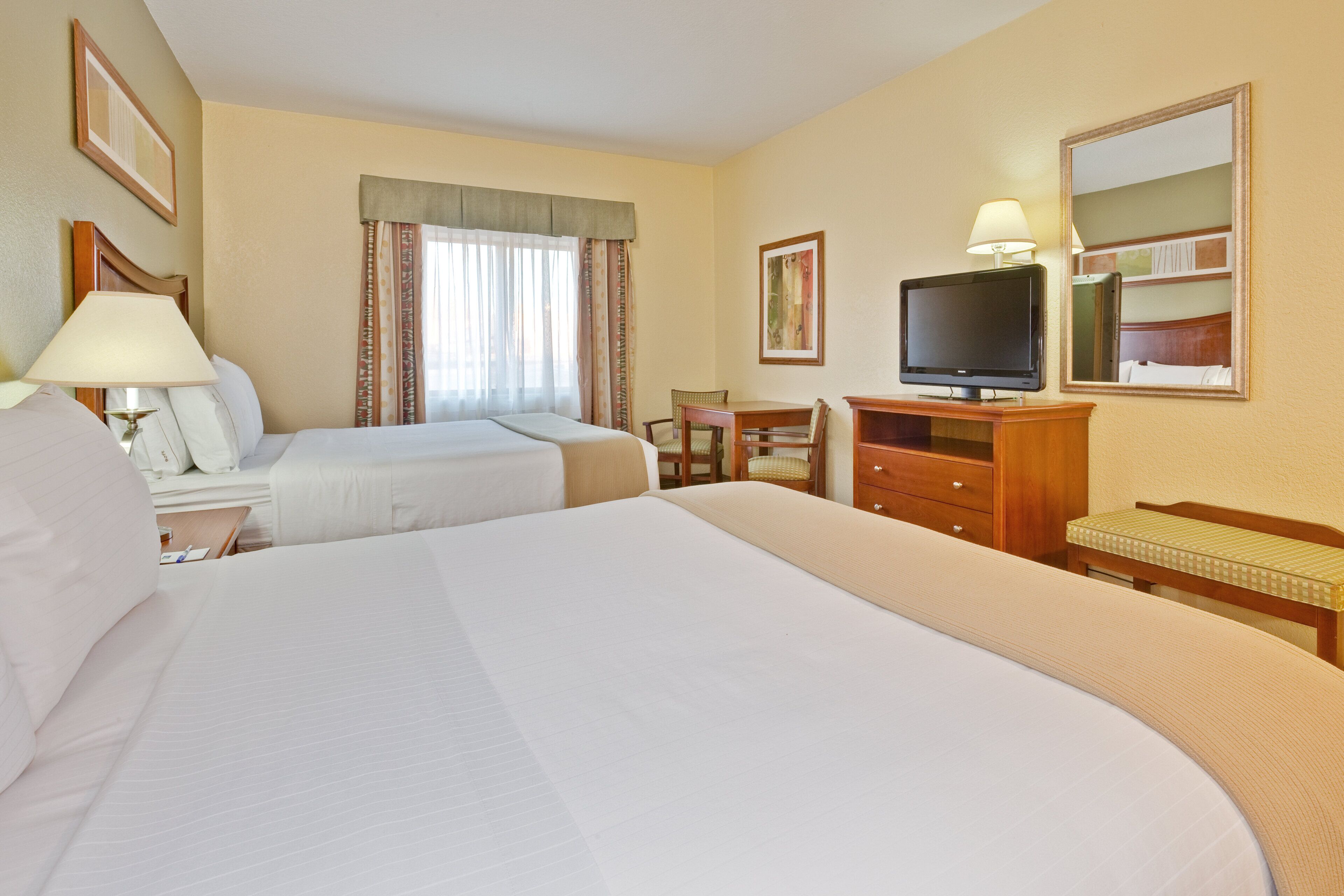 Habitación de hotel con dos camas, televisión, escritorio con lámpara y una silla.