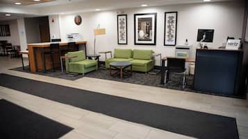 A hotel lobby with a reception desk, green sofas, a coffee table, and a small dining area.