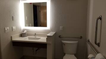 A bathroom with a white sink, mirror, and toilet. There is a handrail on the right side and a towel rack on the left.