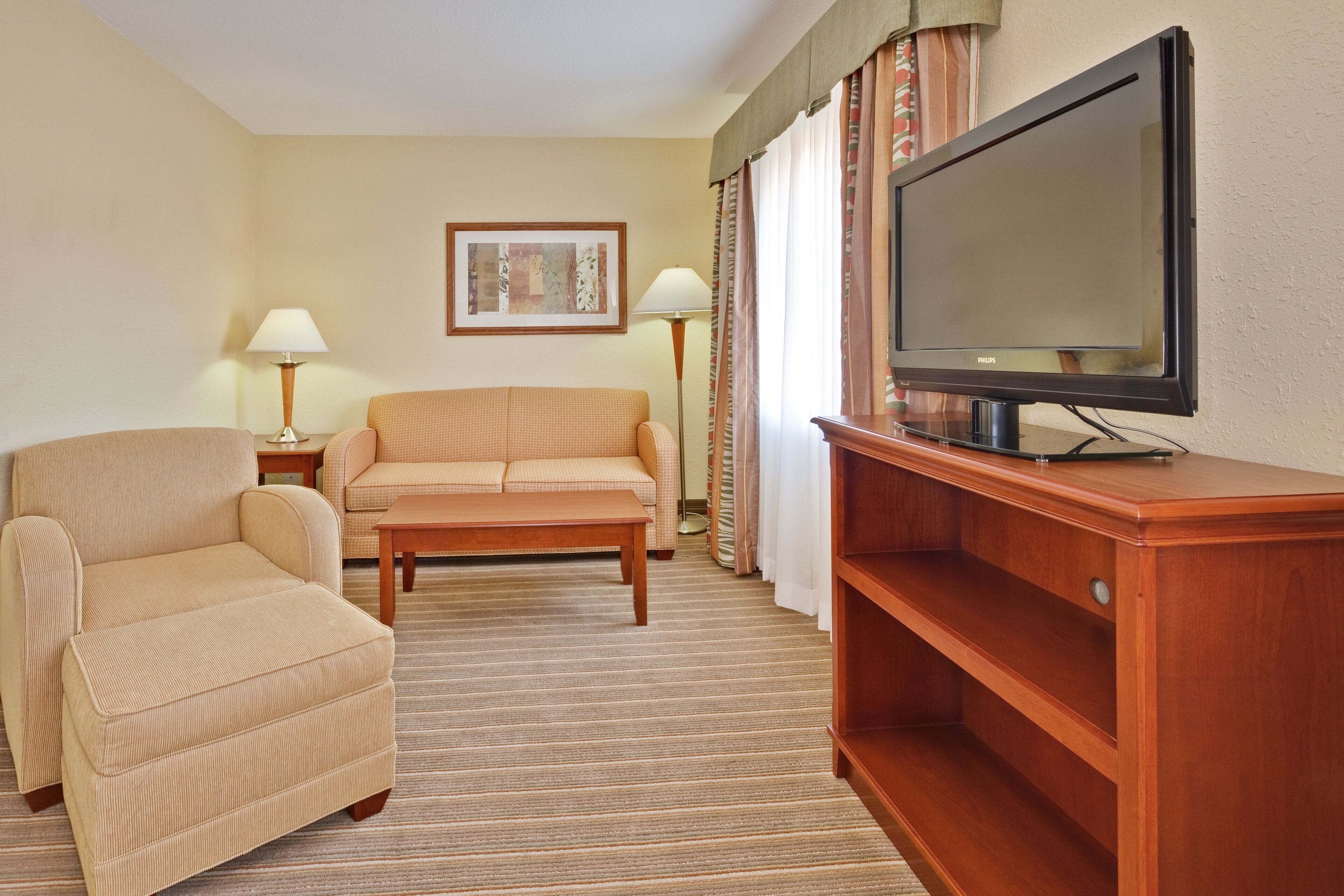 A hotel room with a sofa, armchair, TV, and lamps.