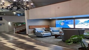Een hotel lobby met modern design, met een zwart-wit schakeerd vloer, een zithoek met fauteuils en een bank, een groot raam met uitzicht op bergen, en een trap naar een hoger niveau.