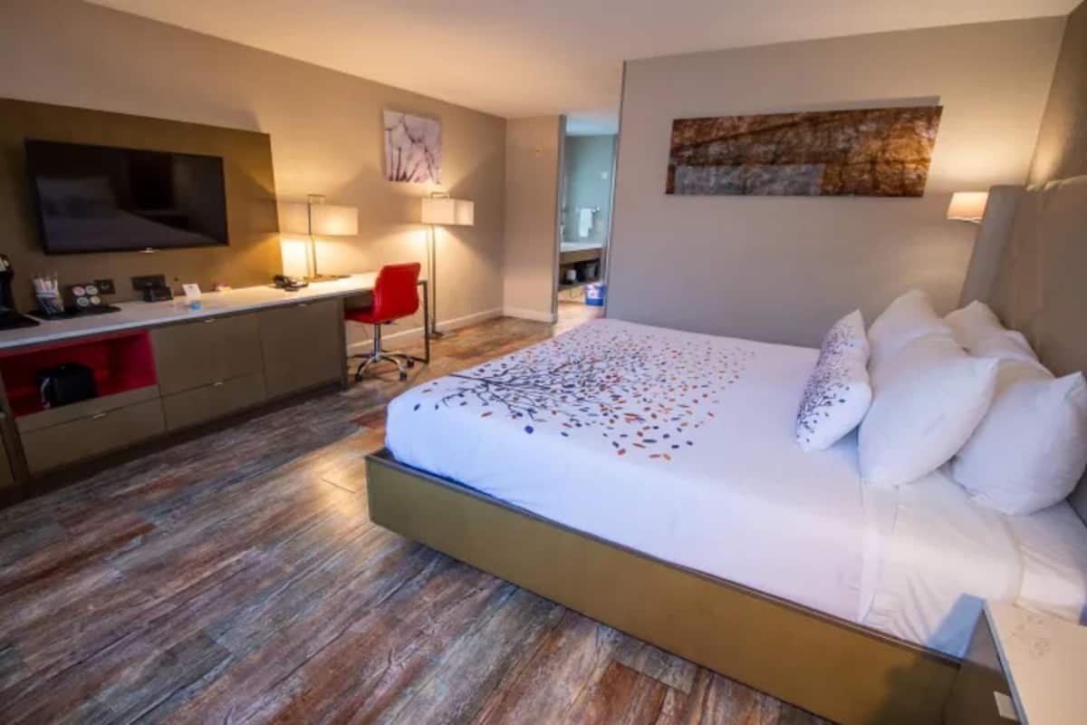 Une chambre d’hôtel avec un grand lit, un bureau avec une chaise, un téléviseur à écran plat et un tableau au mur.