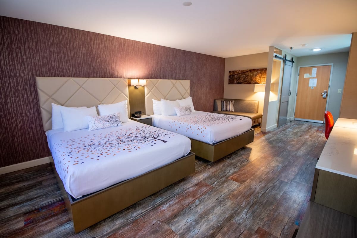 Une chambre d’hôtel avec deux lits, un plancher en bois, un petit bureau et une porte.