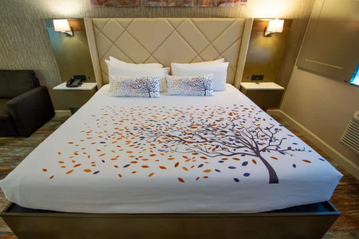 Une chambre d’hôtel avec un grand lit, deux tables de chevet, une petite table, une chaise et une lampe fixée au mur.