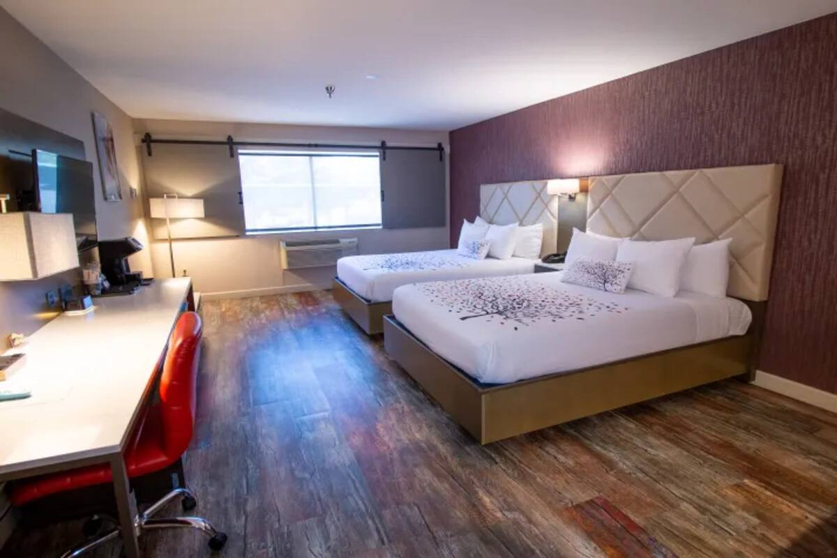Une chambre d’hôtel avec deux lits, un bureau, une chaise et une grande fenêtre.