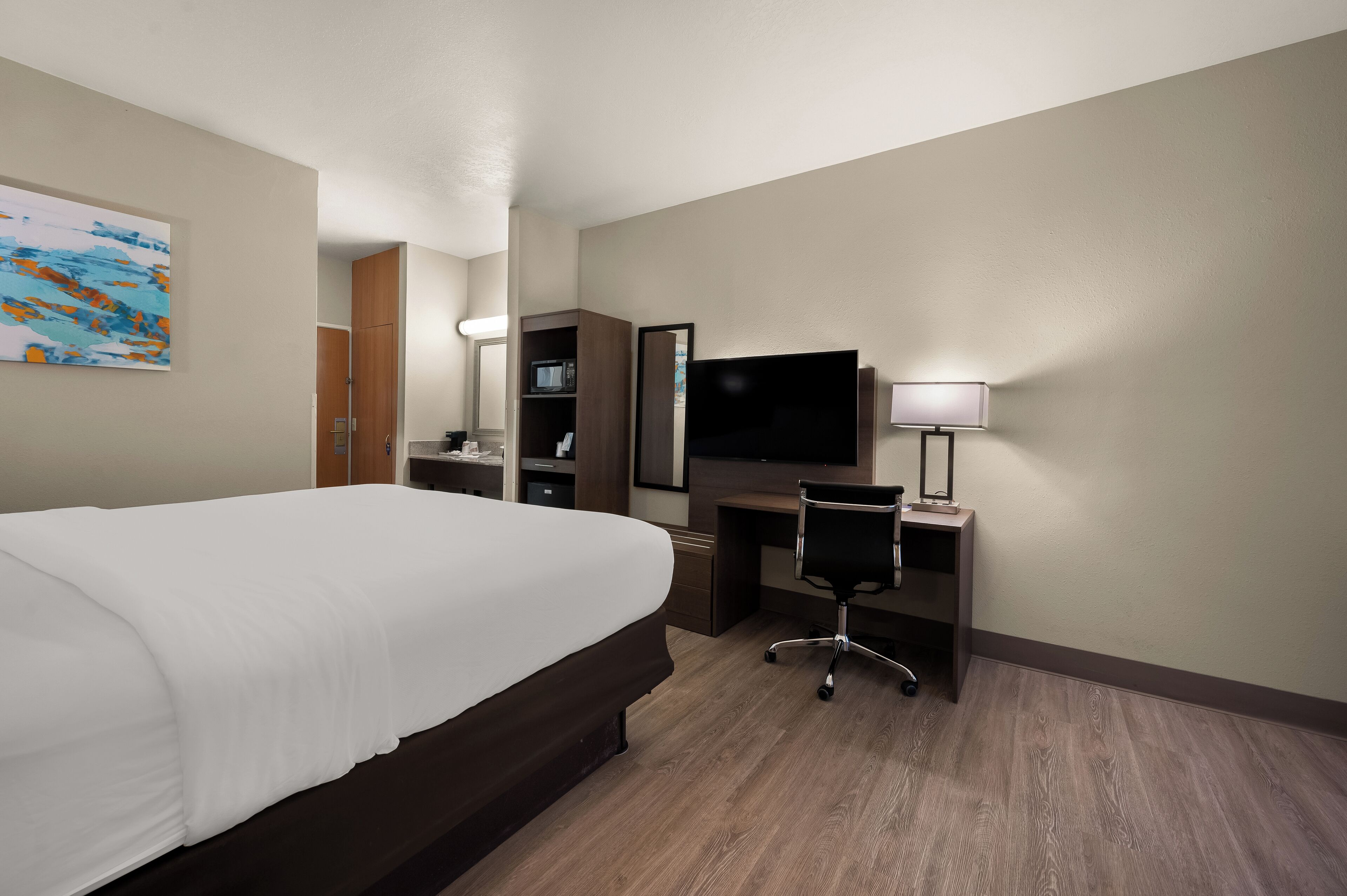 Habitación de hotel con una cama grande, un escritorio con silla, un televisor y una lámpara.