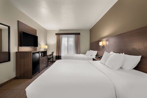 A hotel room with two beds, a desk with a chair, a television, and a window with curtains.